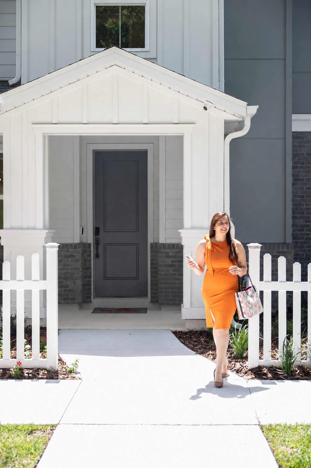 Sheryl Cury walking toward the camera in front of a new home with a white fence
